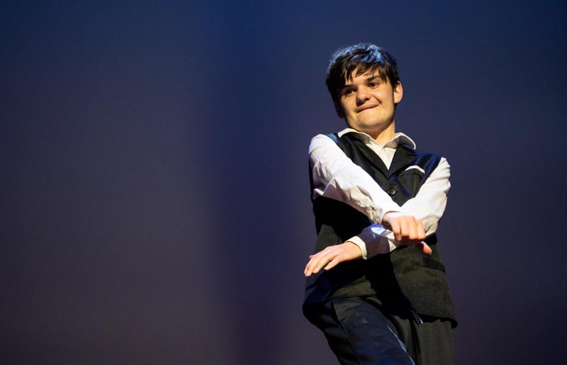Lachlan Oakes performing, arms outstretched. He is wearing a white shirt and black waitcoat and trousers.